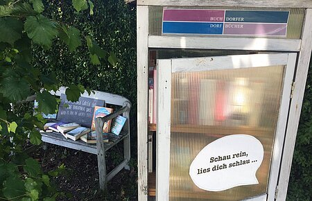 Blick auf den öffentlich zugänglichen Bücherschrank in der Bürgermeister-Rößner-Straße 1 in Buchdorf mit daneben stehender Sitzgelegenheit.