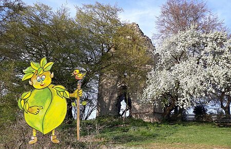 Blick auf eine zwischen Bäumen versteckte Ruine. Links sieht man das grüne, gemalte Waldgeistlein.