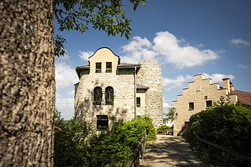 Die Burgruine Altmannstein ist über eine Fußgängerbrücke erreichbar. Links und rechts sind Gebäude, die als Wohnhaus genutzt werden und im Hintergrund ragt der Hungerturm empor. Vom ehemaligen Wohnbau sind nur noch Reste vorhanden.