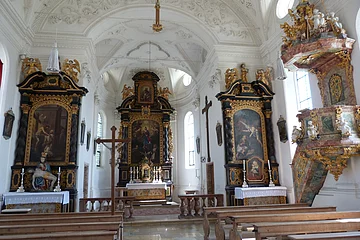 Blick in die helle, lichtdurchflutete Schlosskirche. Vorne in der Mitte der Hauptaltar, links und rechts die Seitenaltäre sowie ganz rechts im Bild die Kanzel.