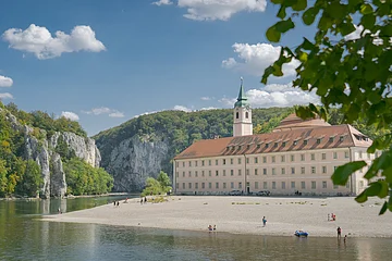 Das Kloster Weltenburg mit seinem Kieselstrand und der Donau, die  im Hintergrund durch den Donaudurchbruch hindurchfließt.