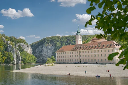 Das Kloster Weltenburg mit seinem Kieselstrand und der Donau, die  im Hintergrund durch den Donaudurchbruch hindurchfließt.