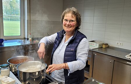Eine Frau steht am Herd und kocht etwas in einem Topf.
