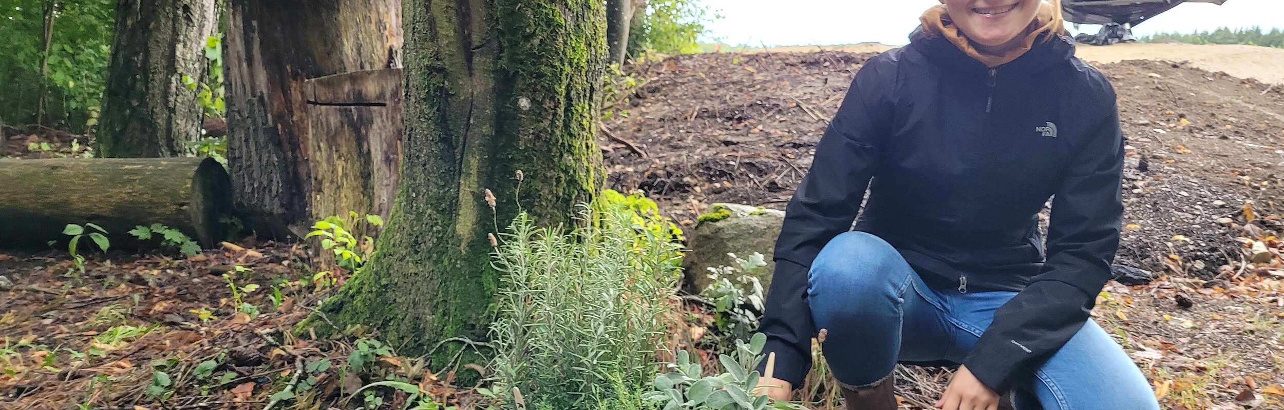 Eine Führerin, die in der Hocke sitzt, zeigt einen vor ihr stehende Korb voll mit Kräutern.