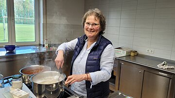 Eine Köchin beim Zubereiten der Wildpflanzen Eine Frau steht am Herd und kocht etwas in einem Topf.