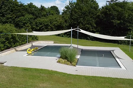 Rechteckiger Pool mit Abdeckung, umgeben von Rasen und Bäumen, mit Sonnensegeln und gelbem Schwimmtier.