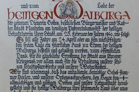 Urkunde von 1946 von Bürgermeister und Rat der Stadt Monheim Ein handgeschriebenes Dokument mit dekorativen roten und schwarzen Buchstaben, das eine religiöse Widmung enthält. Hierin gelobt der Bürgermeister sowie der Rat der Stadt Monheim, ein alljährliches Dankamt zu Ehren der Heiligen Walburga abhalten zu lassen, für die Verschonung der Stadt im Zweiten Weltkrieg.