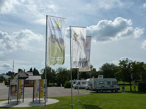 Die Geopark Infostelle mit Flaggen und im Hintergrund die Wohnmobile auf dem Wohnmobilstellplatz in Monheim.