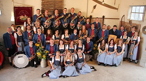 Gruppe von Menschen eines Musikvereins in traditioneller Kleidung mit Musikinstrumenten in einem Raum.