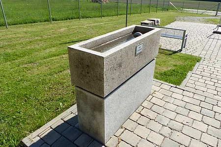 Kneipp Gesundheitsanlage Monheim - Armbecken Armbecken der Kneipp Gesundheitsanlage in Monheim auf gepflastertem Weg neben einer Wiese, mit einem Wasserhahn an der Oberseite.