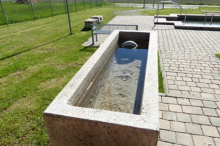 Kneipp Gesundheitsanlage Monheim - Armbecken Steinbecken der Kneippanlage in Monheim mit klarem Wasser auf gepflastertem Platz, im Hintergrund Wiese und Zaun.