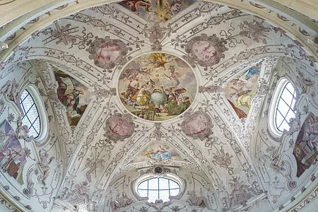 Deckenfresko mit religiösen Szenen und Ornamenten in einer Kirche, umgeben von Fenstern und Stuckverzierungen.