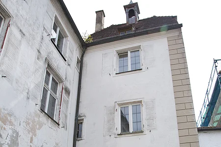 Historisches Stadttor mit Durchfahrt entlang einer Kopfsteinpflasterstraße. Das Tor und das Gebäude links daneben mit einer weiß verputzten Fassade und Verkehrsschildern rechts am Torbogen. Vor dem Tor ein kleines bepflanztes Beet.