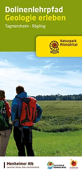 Titelseite des Flyers "Dolinenlehrpfad - Geologie erleben" zum Rundwanderweg in der Monheimer Alb. Der Titel in weißer und gelber Schrift auf geschrieben auf einem grünen Hintergrund. Darunter der Text "Tagmersheim-Rägling" und rechts davon das Logo des Naturparks Altmühltal. Auf dem Foto: links zwei Wanderer mit Rucksäcken von hinten, blicken auf eine grüne Landschaft mit Wiesen und Wald, unter blauem Himmel.
