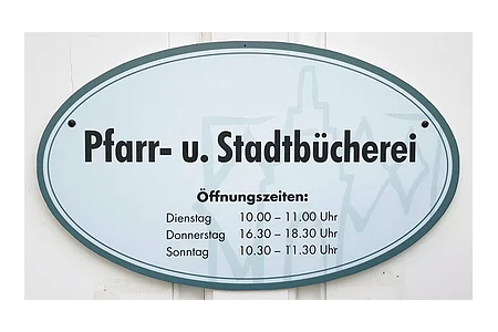 Schild mit Öffnungszeiten der Pfarr- und Stadtbücherei, Dienstag 10-11 Uhr, Donnerstag 16:30-18:30 Uhr, Sonntag 10:30-11:30 Uhr.