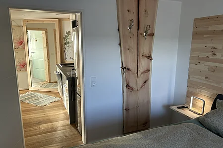 Blick von Schlafzimmer mit Holzbett und Nachttisch in Flur mit Holzboden und großem Spiegel an Wand