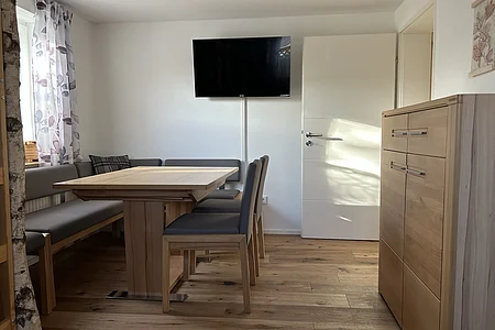 Esszimmer mit Holztisch, grauen Stühlen, Eckbank, TV an weißer Wand und Sideboard aus Holz