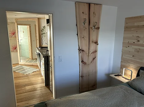 Blick von Schlafzimmer mit Holzbett und Nachttisch in Flur mit Holzboden und großem Spiegel an Wand