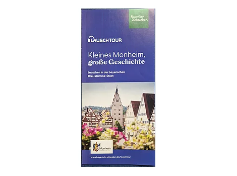 Flyer zur Lauschtour in Monheim mit dem Titel „Kleines Monheim, große Geschichte“ und Bild darunter von einer historischen Altstadt mit Fachwerkhäusern und Turm, im Vordergrund unscharfe pinke Blumen. Oben rechts im Eck das Logo von Bayerisch Schwaben und unten links im Eck das Logo der Stadt Monheim.