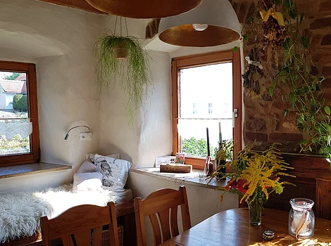 Esszimmer mit Holztisch, Stühlen, Fensterbank mit Kissen, Pflanzen und Blumenstrauß auf dem Tisch