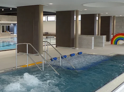 Innenansicht eines Schwimmbads mit Whirlpool, Schwimmbecken und Wasserspiel in Regenbogenform