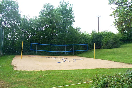 Sandvolleyballfeld mit blauem Netz und grüner Umgebung, keine Personen sichtbar.