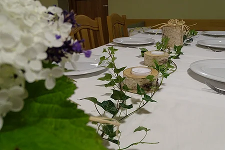 Esstisch mit weißer Tischdecke, Holzkerzenhaltern, Efeuranken und weißen Tellern mit Besteck.