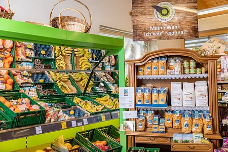Supermarktregal mit Obst, Gemüse und regionalen Produkten, darüber ein Schild mit Aufschrift „Meine Wahl: Ich kauf‘ regional!“