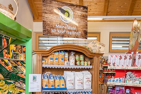 Verkaufsregal mit regionalen Produkten, darunter Nudeln, Getränke und Kartoffeln in einem Laden mit Holzdecke.