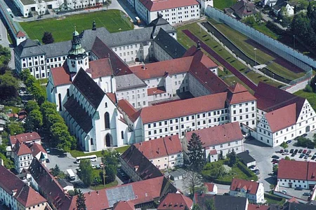 Luftaufnahme eines historischen Gebäudekomplexes mit Kirche, umgeben von Wohnhäusern und Straßen.