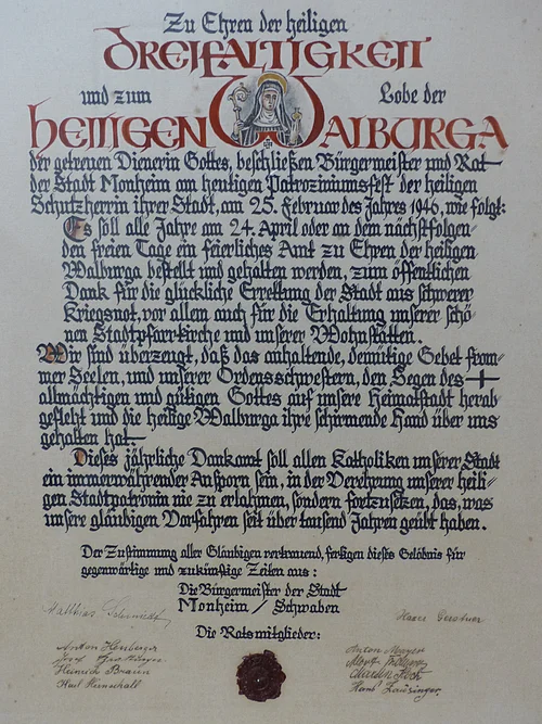 Dankamt-Urkunde von 1946 von Bürgermeister und Rat der Stadt Monheim Ein handgeschriebenes Dokument mit dekorativen roten und schwarzen Buchstaben, das eine religiöse Widmung enthält. Hierin gelobt der Bürgermeister sowie der Rat der Stadt Monheim, ein alljährliches Dankamt zu Ehren der Heiligen Walburga abhalten zu lassen, für die Verschonung der Stadt im Zweiten Weltkrieg.