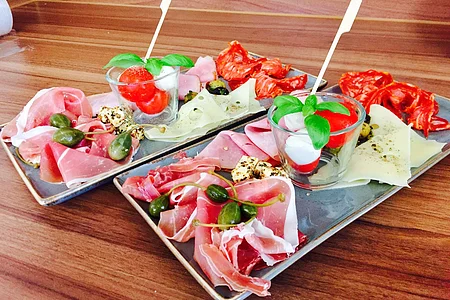 Zwei gleich angerichtete Teller mit Aufschnitt, Käse, Schinken, Tomaten, Mozzarella und Basilikum auf Holzoberfläche.