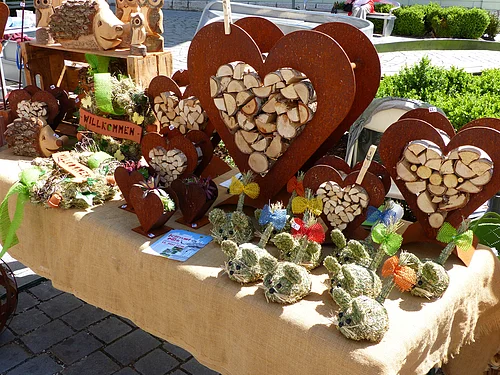 KunstHandWerkMarkt 2018 in Monheim Marktstand mit Holzherzen, Holztieren und dekorativen Figuren aus Stroh auf einem mit Leinen bedeckten Tisch.