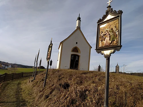 Kleine weiße Kapelle, die Kalvarienbergkapelle in Wittesheim, auf einem Hügel mit mehreren Kreuzwegstationen entlang eines Weges im Vordergrund.