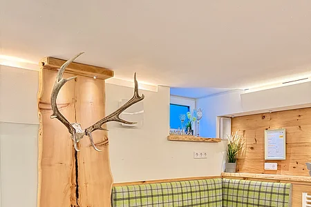 Eckbank mit grün kariertem Polster, Holzwand mit Geweih und kleinen Fenstern im modernen Raum