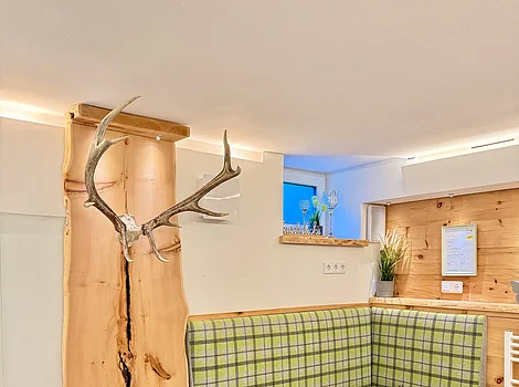 Ferienwohnung Zirben-Spa Eckbank mit grün kariertem Polster, Holzwand mit Geweih und kleinen Fenstern im modernen Raum