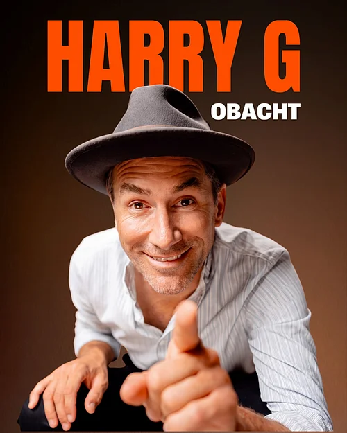 Harry G. "Obacht"- in der Stadthalle Monheim Mann mit grauem Hut und weißem Hemd zeigt mit Finger nach vorne, Text „HARRY G OBACHT“ im Hintergrund. Veranstaltung in der Monheimer Stadthalle am 26. April 2027